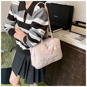 Close-up of pink crossbody bag with silver bow accent and elegant cursive embroidery