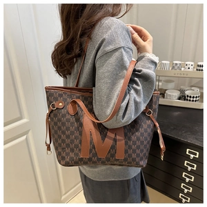 Detail of large brown tote bag with letter print and leather M patch on shoulder