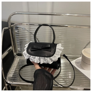 Detailed view of black leather handbag with white lace trim and bow knot decoration