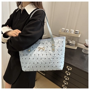 Detail of light blue tote bag with embroidered black bows and a gold metal bow clasp