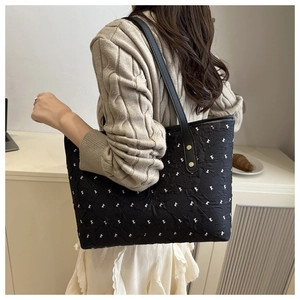 Detail view of large black tote bag with white bow print and leather shoulder straps