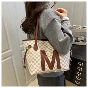 Side view of beige canvas tote bag with brown letter print and leather straps