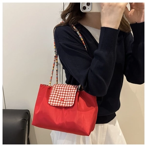 Close-up of red tote bag featuring colorful woven straps and a red checkered flap detail