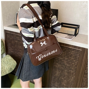 Close-up of deep brown patent leather tote featuring a white bow and embroidery detail