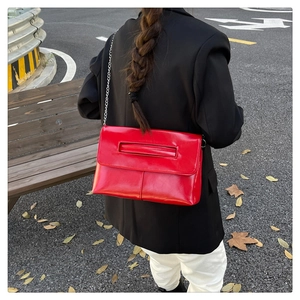 Détail du sac enveloppe rouge en cuir verni avec chaîne argentée et poignée intégrée