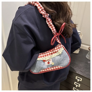 Close-up of denim shoulder bag featuring red plaid straps and lace decorative details