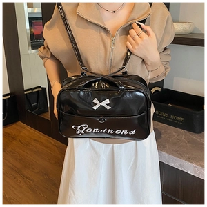 Detail of glossy black patent leather tote with white bow and cursive letter embroidery