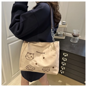 Detail of beige tote bag featuring cat embroidery and silver chain strap design