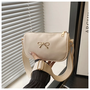 Close-up of cream square bag with gold bow detail and wide adjustable canvas strap