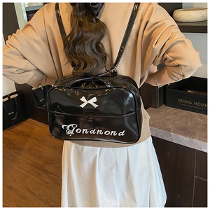 Detail of black glossy backpack with white bow and embroidered lettering on back