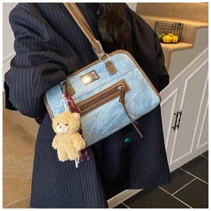 Détail du sac cabas en jean bleu clair avec garniture en cuir brun et breloque ours