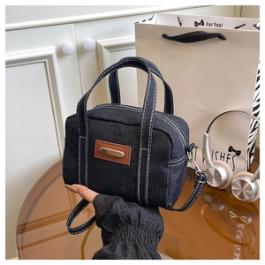 Detail of grey denim handbag with white stitching and brown leather label decoration