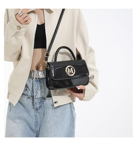 Fashionable black faux leather crossbody bag with golden M emblem shown on a model