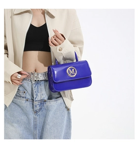 Detail of glossy bright blue patent leather handbag with golden round metal M logo