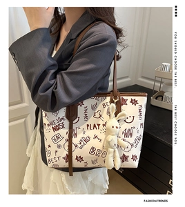 Detail of white graffiti tote bag with brown leather handles and plush bunny charm