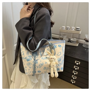 Detail of canvas tote bag featuring blue graffiti prints and a cute rabbit plush charm