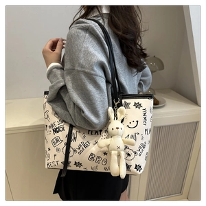 Close-up of white tote bag with black graffiti prints and a plush rabbit pendant detail