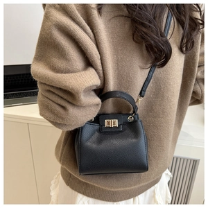 Detail of black pebbled leather bucket bag with gold rectangular clasp and shoulder strap