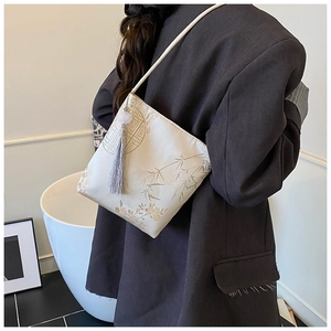Detail of embroidered butterfly bucket bag with satin texture and tassel pendant accessory