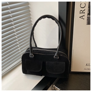 Detail of black suede rectangular handbag featuring symmetric flap pockets and slim handles