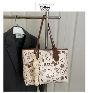 Detail of coffee brown tote with graffiti prints and a cute plush bunny charm pendant