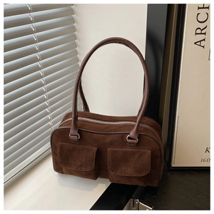 Detail of dark brown shoulder bag featuring dual front flap pockets and round handles