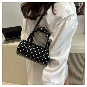 Close-up of black and white polka dot cylinder handbag with high-gloss finish and straps
