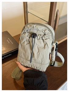Détail d'un sac bandoulière en nylon gris-vert avec broderie et cordon de serrage