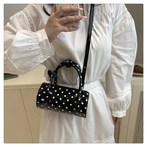 Detailed view of polka dot cylindrical handbag with glossy finish and metal zipper