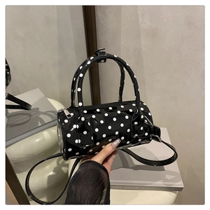 Detailed close-up of a black polka dot patent leather boston bag on a white display stand