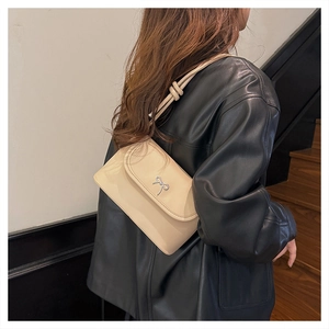 Détail d'un sac à bandoulière crème avec nœud argenté porté par un mannequin en mode