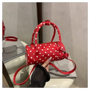 Detailed close-up of a red polka dot cylindrical handbag in glossy patent leather texture