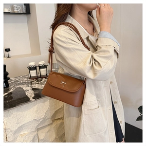 Détail d'un sac bandoulière marron en cuir avec boucle nœud argentée porté sur un trench-coat
