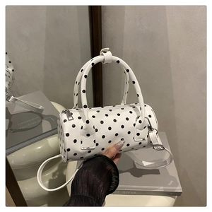 Polished white cylinder bag with black polka dots on a minimalist display stand