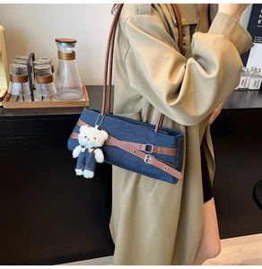 Detail of denim shoulder bag with brown leather straps and cute plush teddy bear charm