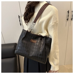 Detail of black quilted tote bag with brown leather strap and silver chain links