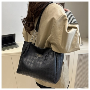 Detail of black tote bag with quilted texture and chain strap in office setting