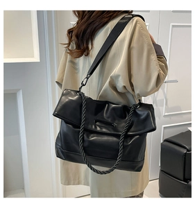 Detail of a large black PU leather tote bag showing rope handles and wide nylon shoulder strap