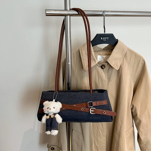 Detail of denim baguette bag with brown leather straps and a cute plush bear charm