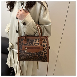 Detail of leopard print tote bag with brown leather trim and decorative front zipper pocket