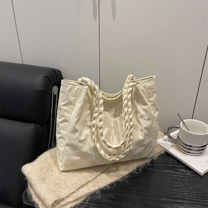 Chic cream-colored quilted tote bag with bear pattern and woven handles on a desk