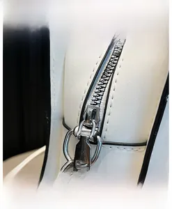 Detail view of the silver metal zipper and black trim on white leather crossbody bag