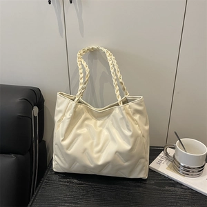 Creamy white quilted tote bag with a unique woven handle on a minimalist surface