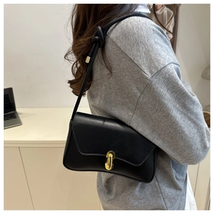 Detail of minimalist black leather shoulder bag with gold clasp and knotted strap