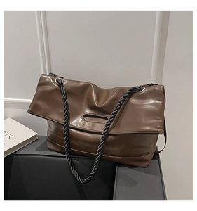 Detail of a brown PU leather tote bag with black twisted rope handles on a grey stand
