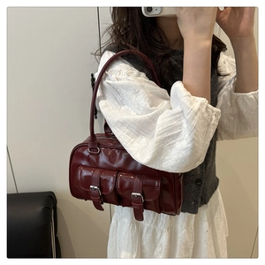 Detail of burgundy glossy leather handbag featuring two buckled flap pockets and silver buckles