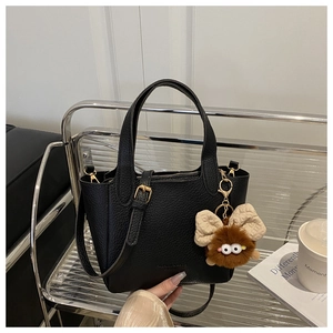 Detail of black lychee grain leather tote bag with monster charm and shoulder strap