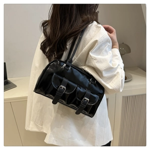 Detail view of glossy black faux leather shoulder bag with buckle pockets on a model