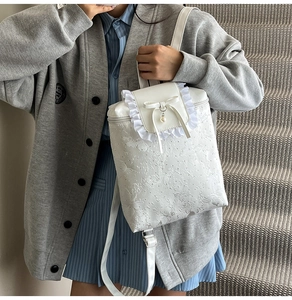 Detail of white backpack with floral embroidery, pearl bow charm, and ruffled trim