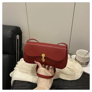 Detail of red faux leather flap bag with gold metal buckle on a white cloth backdrop